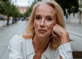 Elegant mature woman in white shirt poses confidently on an urban street, showcasing timeless beauty.